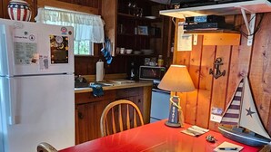 Una cocina compacta con armarios de madera, una mesa roja y un pequeño comedor.