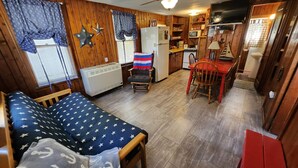 Un espacio habitable compacto con cama, una mesita, una silla, kitchenette y ventilador de techo.