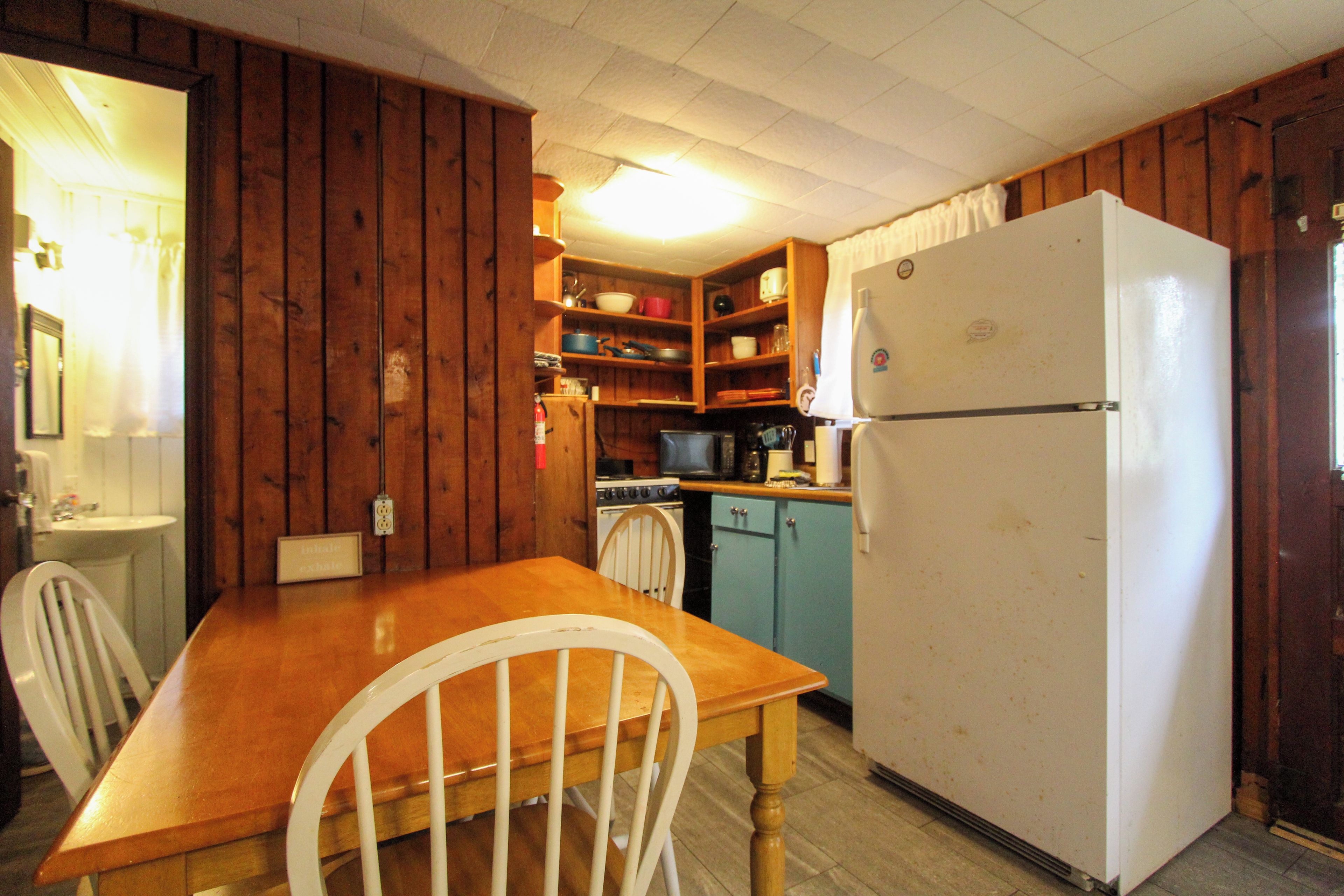 A compact kitchen with wooden cabinets, a white refrigerator, a stove, and a dining table with chairs.