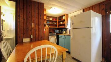 A compact kitchen with wooden cabinets, a white refrigerator, a stove, and a dining table with chairs.