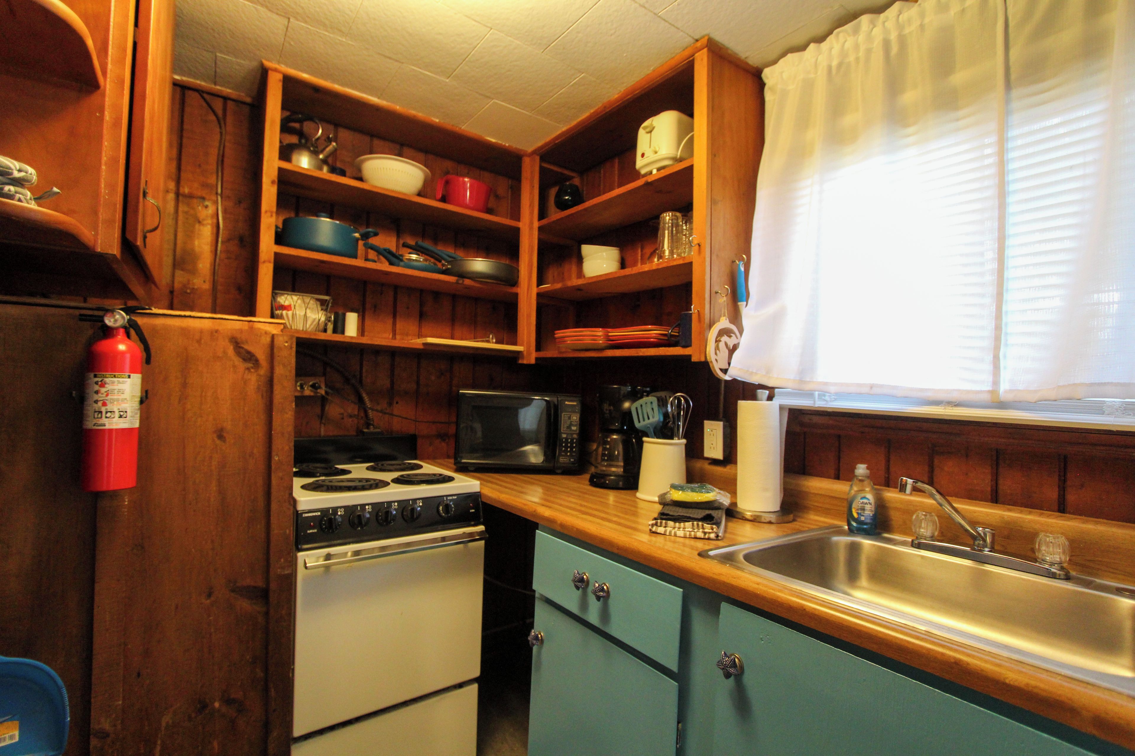 A compact kitchen with wooden cabinets, a stove, a microwave, and a sink.