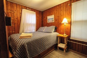 Una camera da letto con un letto, un comodino con una lampada, una finestra con tende e un quadro appeso al muro.