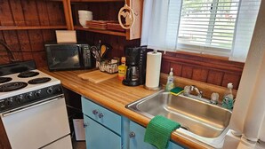 Cocina pequeña con estufa, microondas, lavamanos y armarios de madera.