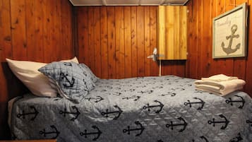 Un dormitorio con cama, almohadas, una manta, un cuadro enmarcado y una toalla doblada.