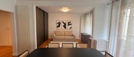 Un salon moderne avec une grande table noire, deux canapés et un coin repas avec des chaises. On y trouve des œuvres d'art abstrait accrochées aux murs, ainsi qu'une fenêtre avec des rideaux.