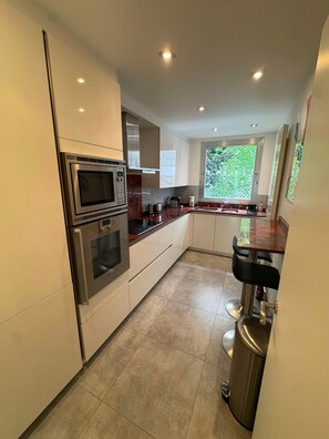 A modern kitchen with stainless steel appliances, a marble countertop, and a window providing a view of greenery. - UrbanFlat 229 - Appartement Bail Mobilité Paris 16 (Paris)