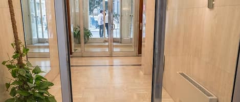 Un moderno vestíbulo de hotel con entrada por puerta de vidrio, una planta en maceta y un radiador en la pared.