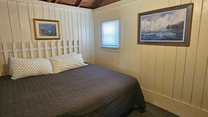 Un dormitorio con cama, dos almohadas, una ventana y dos cuadros en la pared.