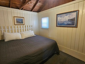 Une chambre à coucher avec un lit, deux oreillers, une fenêtre et deux tableaux encadrés accrochés au mur.