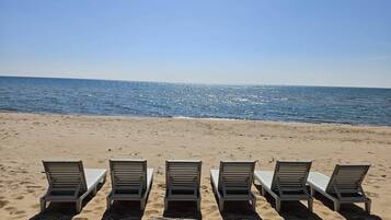 Ein Strand mit fünf Liegestühlen, die in einer Reihe zum Meer ausgerichtet sind.