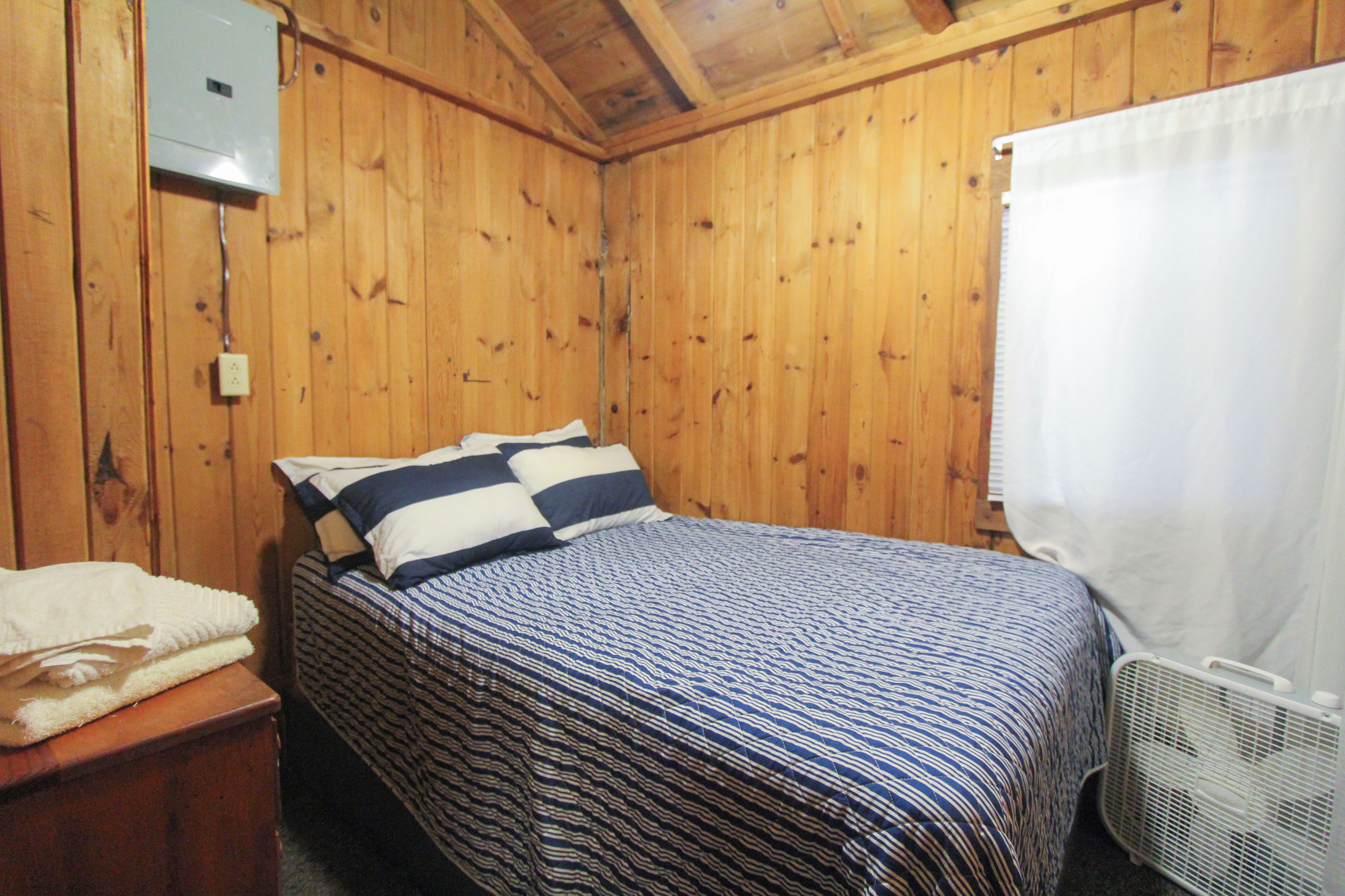 A single bed with striped bedding in a wooden room with a white curtain on the window.