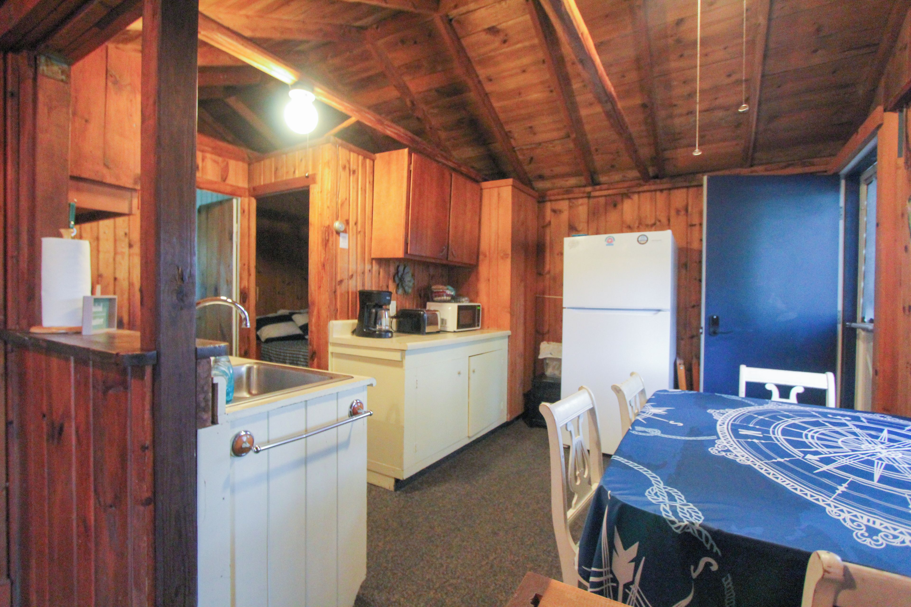 A cabin-style kitchen with wooden walls, a white refrigerator, a sink, and a table with chairs.
