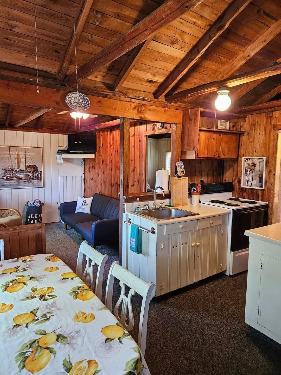 A cozy cabin interior with a dining table, a sofa, a kitchenette, and a ceiling fan.