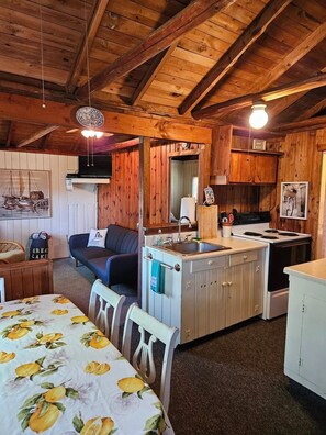Interior acogedor de una cabaña con mesa de comedor, sofá, kitchenette y ventilador de techo.