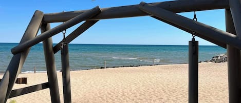 Et gyngestativ i træ med udsigt over en sandstrand og havet i baggrunden.