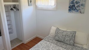 Un dormitorio con cama, armario, ventana con cortina y un cuadro en la pared.