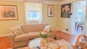 Una sala de estar con un sofá color beige, una mesa de centro de vidrio y una silla de mimbre.