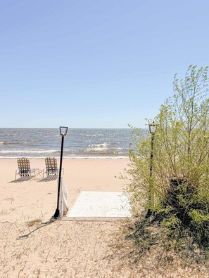 Una platja amb dues cadires metàl·liques i un fanal, un camí blanc que condueix a l'aigua, i una vista clara de l'oceà.