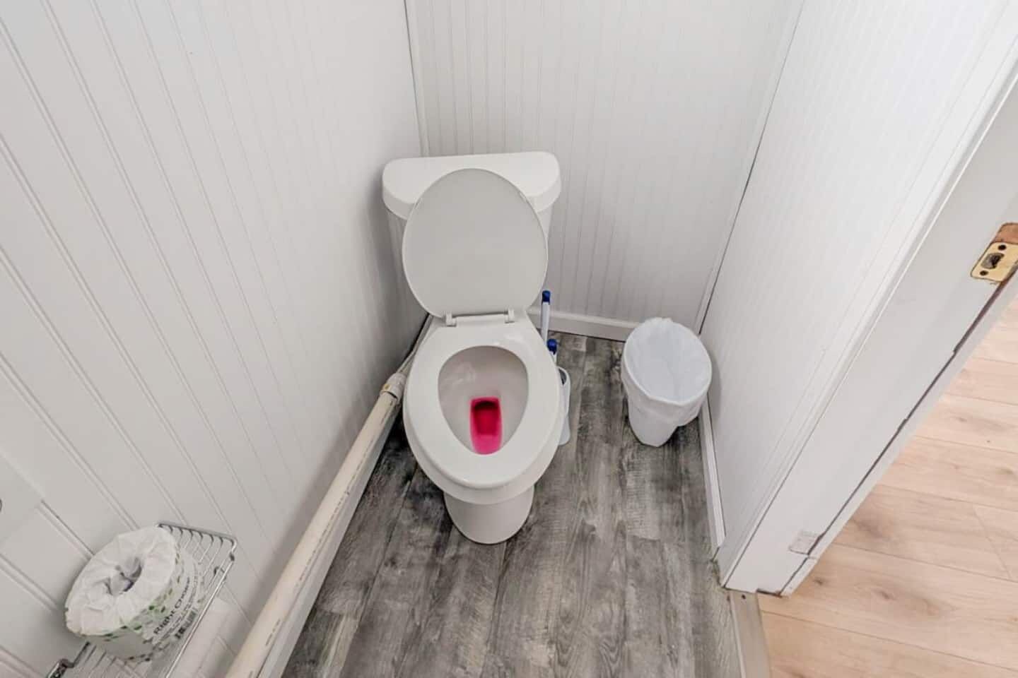 A small bathroom with a toilet, a trash bin, and a toilet brush.