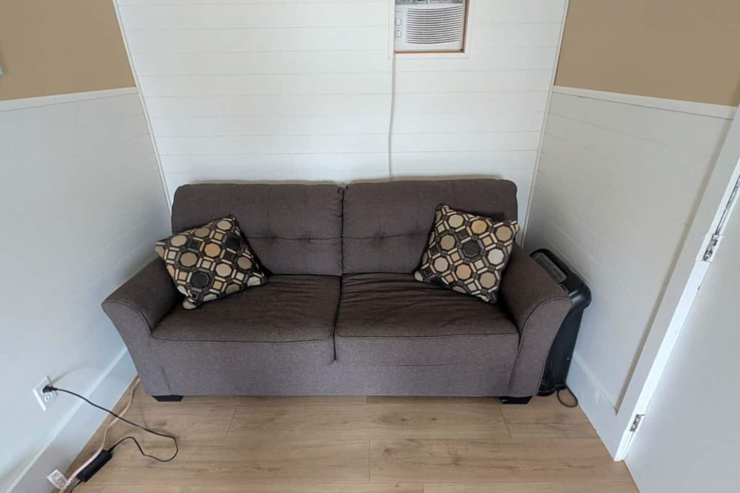 A brown sofa with patterned cushions in a room with wooden flooring and white walls.