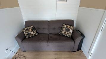 A brown sofa with patterned cushions in a room with wooden flooring and white walls.