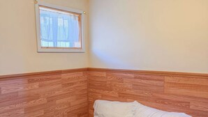Una cama individual con cabecera de madera y una ventana con cortina blanca.