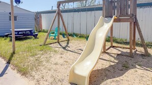 Un patio trasero con un parque infantil de madera, que incluye un columpio, un tobogán, una mesa de picnic y una antena parabólica.
