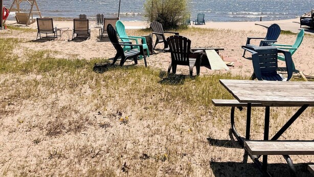 Un área de estar frente a la playa con sillas y una mesa de picnic, con vista al océano.
