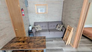 Una habitación pequeña y compacta con sofá, una mesa de madera, extintor y un pequeño calentador.