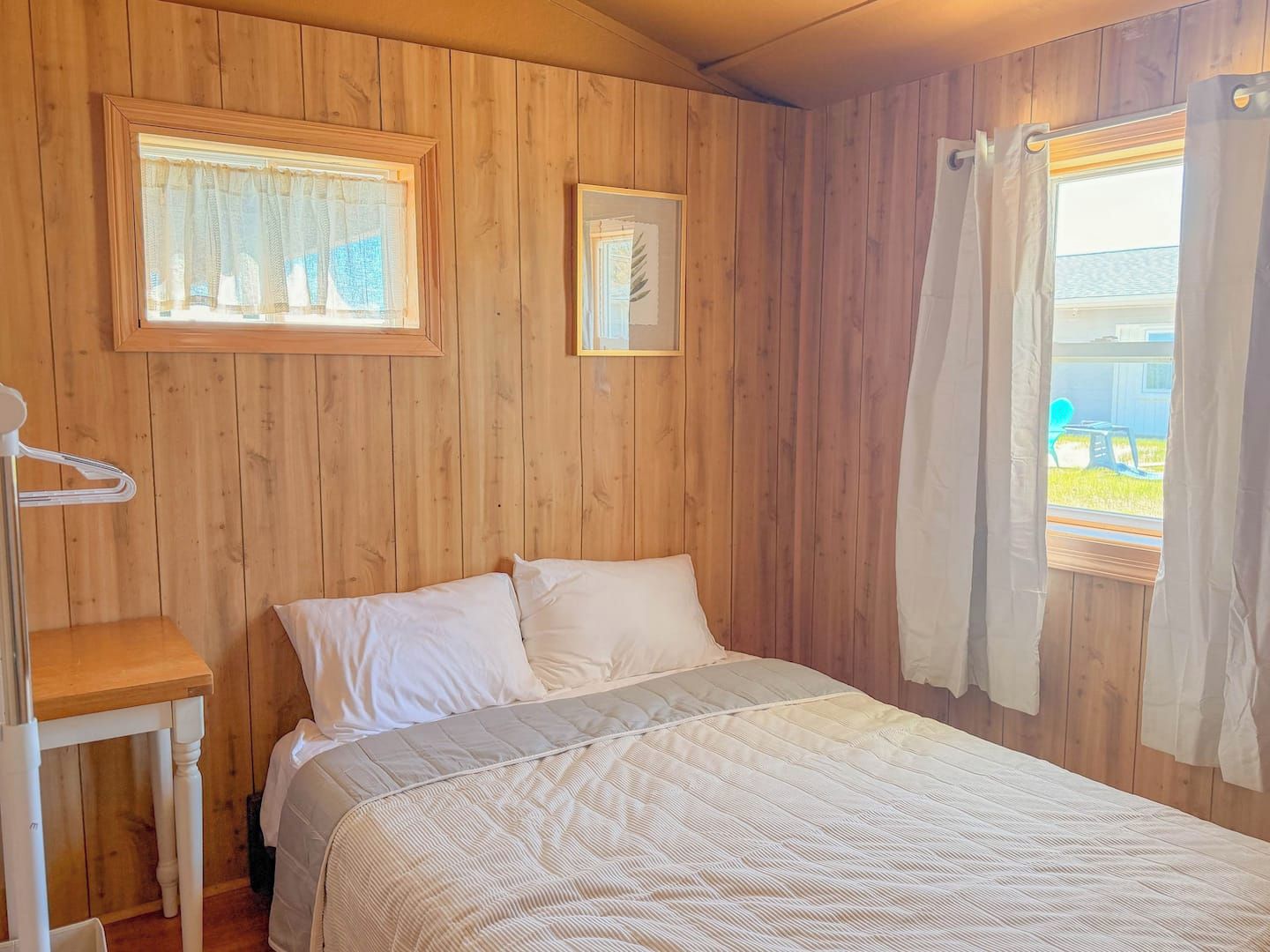 Ein Zimmer mit Holzvertäfelung, einem Bett, einem kleinen Tisch und einem Fenster mit Vorhängen.