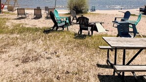 Un área de estar frente a la playa con sillas y una mesa de picnic, con vista al océano.