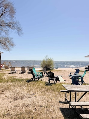 Een zitgedeelte aan het strand met stoelen en een picknicktafel, met uitzicht op de oceaan.