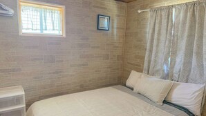 Un dormitorio con cama, ventana con cortinas, un cuadro colgado en la pared y cabecera de madera.