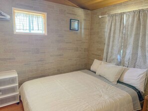 Een slaapkamer met een bed, een raam met gordijnen, een aan de muur bevestigd fotolijstje en een houten hoofdbord.