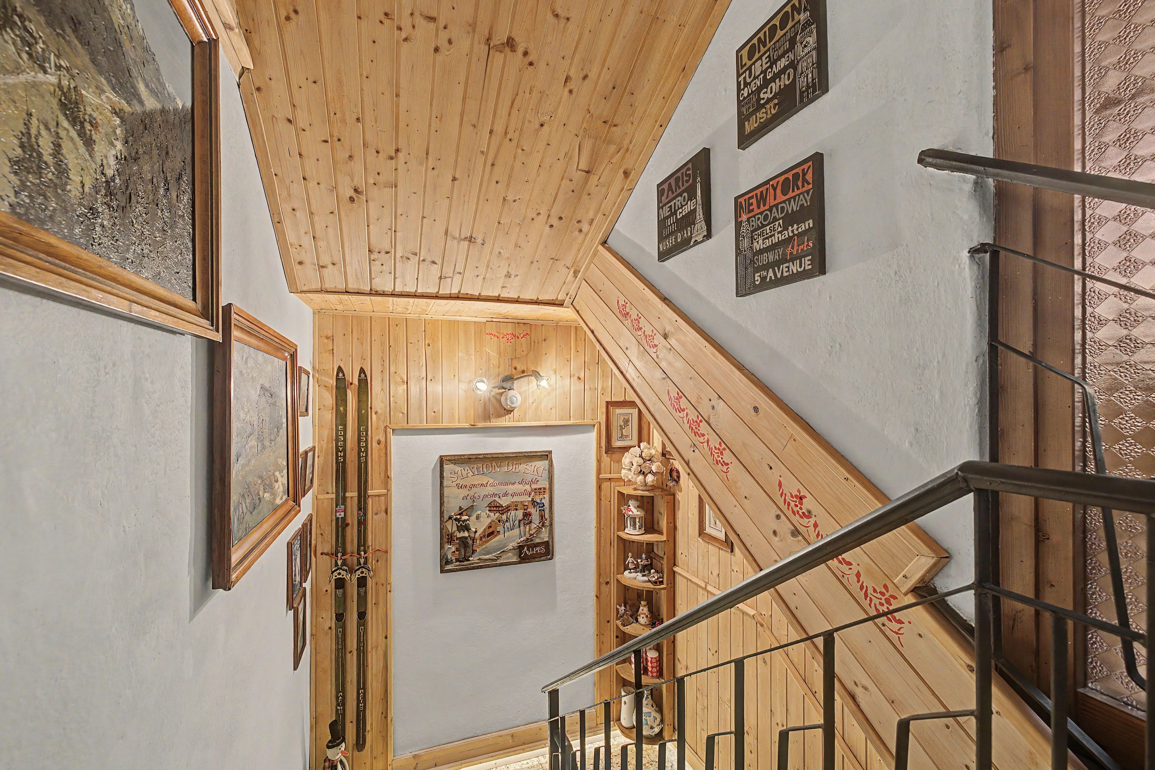 Eine Treppe mit Holzwerteln und einer Holzbalkendecke. An den Wänden befinden sich Bilder und Schilder in Rahmen.