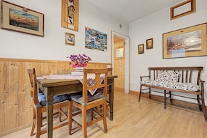 A dining area with a wooden table, chairs, and a bench. There are framed pictures on the walls.