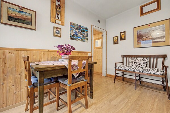 A dining area with a wooden table, chairs, and a bench. There are framed pictures on the walls.