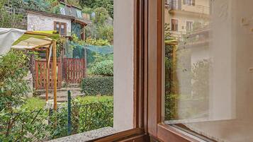 Blick aus dem Fenster auf einen Garten mit einer Holz-Pergola, einem Holzzaun und verschiedenen Pflanzen.