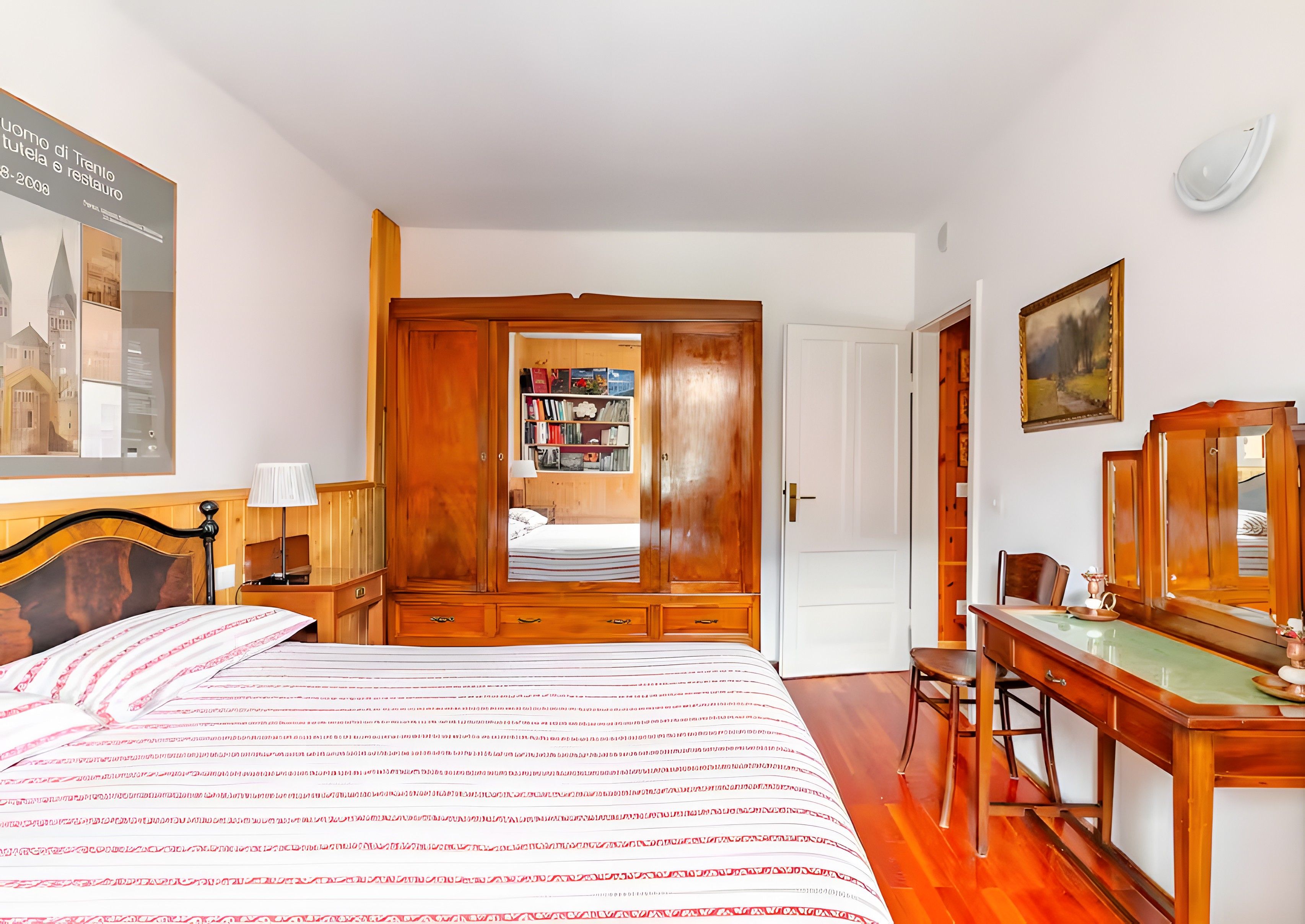Une chambre à coucher comprenant un lit, une armoire en bois, un bureau, une chaise et une bibliothèque.