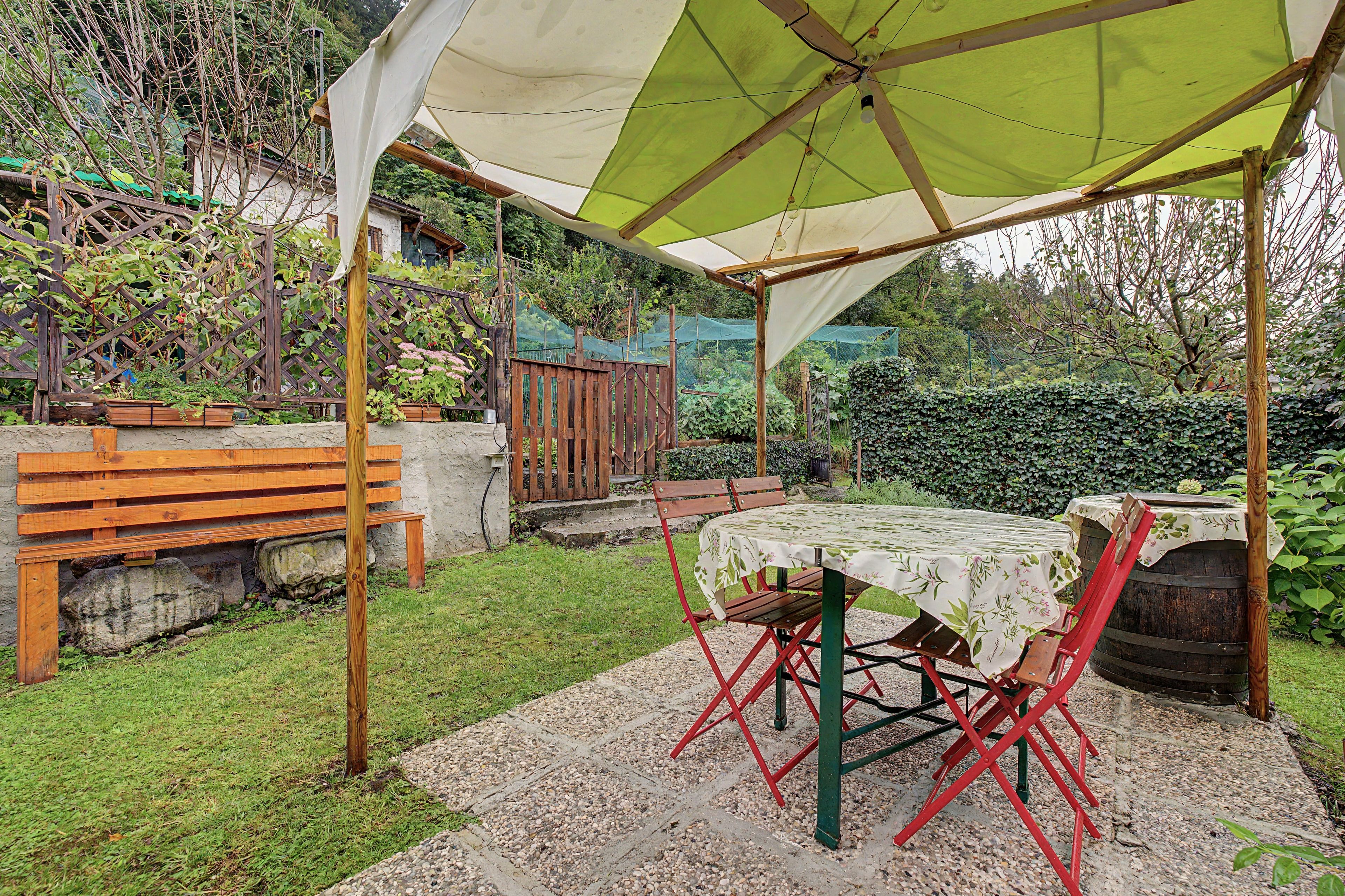 Un área de estar al aire libre cubierta con una mesa y sillas, rodeada de un jardín.