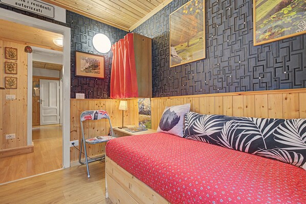 A bedroom with a bed, a chair, a lamp, and a wall with patterned wallpaper.