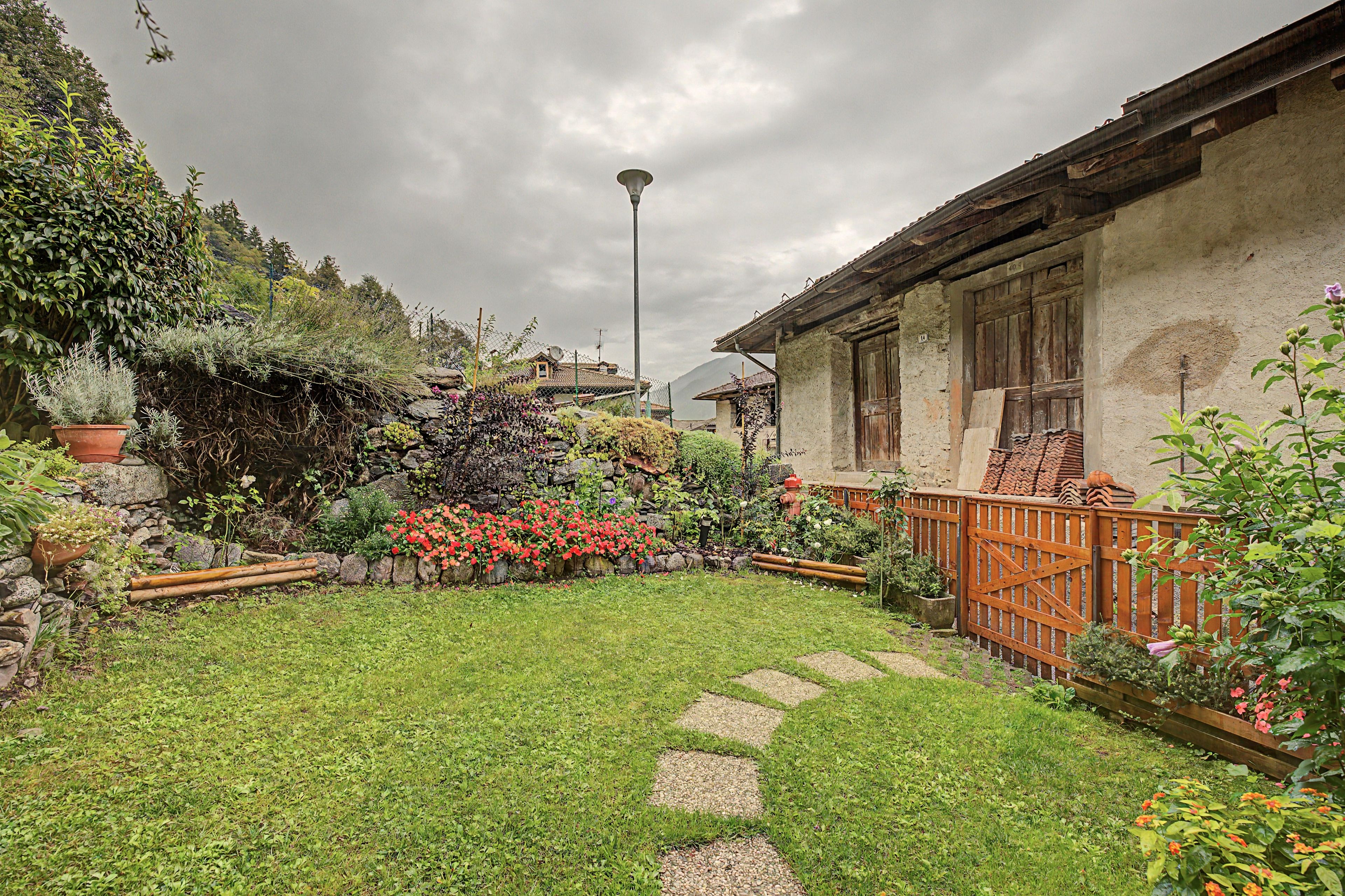 Un giardino con un vialetto in pietra che conduce a una casa rustica con una recinzione in legno.