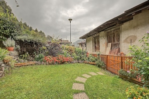 A garden with a stone pathway leading to a rustic house with a wooden fence.