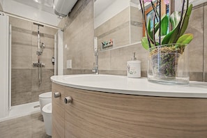 A modern bathroom with a curved vanity, a glass container with green plants, a white toilet, and a shower area.