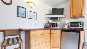 A compact kitchen with a microwave, toaster, and a small refrigerator. There is a wooden chair with a striped cushion and a wall-mounted shelf above the counter. - A budget-friendly, freshly renovated studio at Sunnyside, just steps from the lake. (Greenbush)