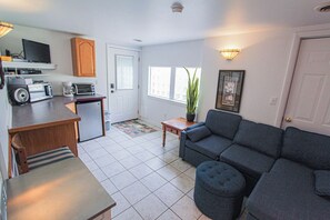 A compact living space with a kitchenette, a sofa, a coffee table, and a potted plant. - A budget-friendly, freshly renovated studio at Sunnyside, just steps from the lake. (Greenbush)