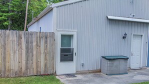 A single-story building with a white door, a small window, and a metal shed with a green roof. - A budget-friendly, freshly renovated studio at Sunnyside, just steps from the lake. (Greenbush)