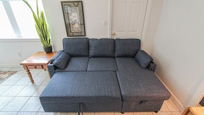 A sectional sofa in a room with a tiled floor, a small wooden table, and a potted plant. - A budget-friendly, freshly renovated studio at Sunnyside, just steps from the lake. (Greenbush)