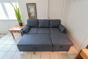 A sectional sofa in a room with a tiled floor, a small wooden table, and a potted plant. - A budget-friendly, freshly renovated studio at Sunnyside, just steps from the lake. (Greenbush)