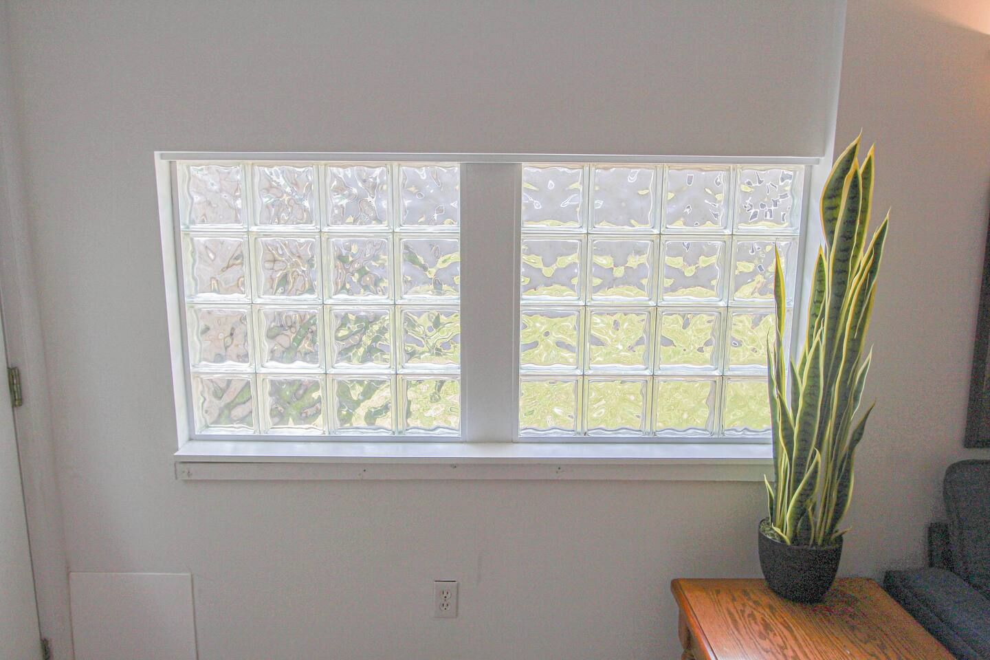 Una habitación con un ventanal de diseño de cuadrícula, una planta en maceta sobre una mesa de madera y un sofá gris.